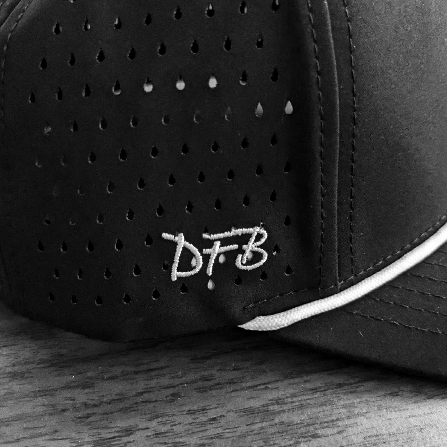 Black perforated cap with 'DFB' logo on a wooden surface